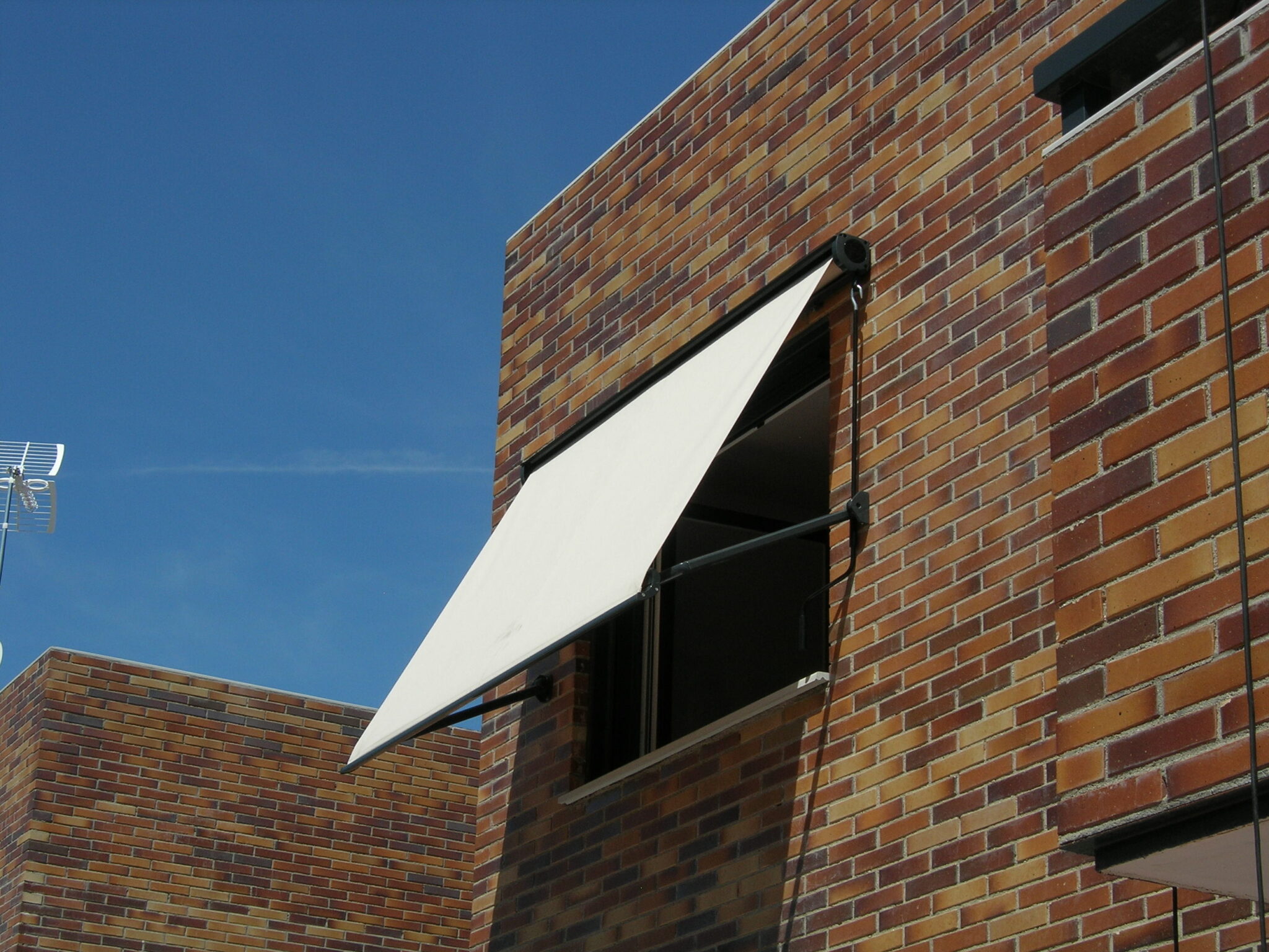 Toldo instalado sobre ventanas en una fachada residencial