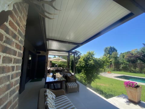 Pérgola bioclimática adosada a la vivienda junto a un jardín