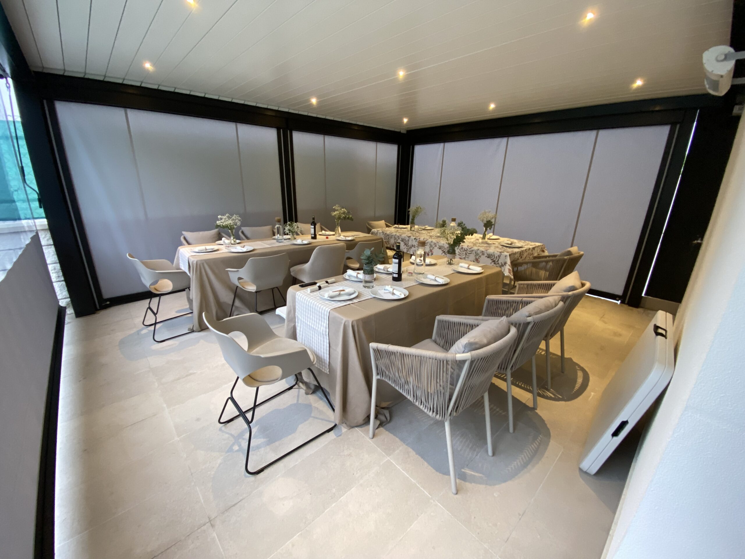 Zona de comedor iluminada bajo la pérgola bioclimática con toldos verticales bajados en Valdemoro