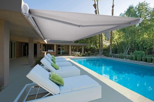 Toldo extensible que da sombra a una terraza junto a una piscina